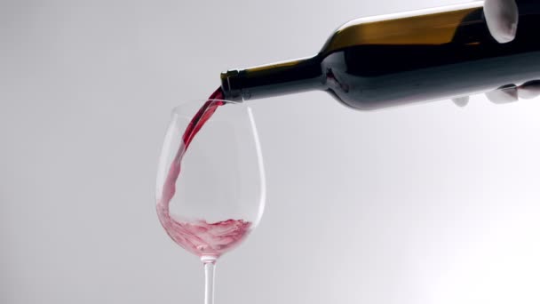 Pouring black, red wine from a clear glass into an glass on a white background — Stock Video