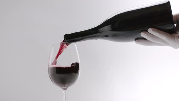 Nalít červené víno do čiré sklenice na bílém pozadí, ve zpomaleném filmu — Stock video