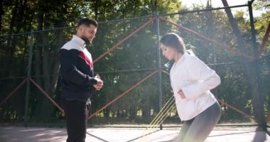 Kişisel antrenörü olan sporcu bir kadın dışarıda direniş bandıyla egzersiz yapıyor.