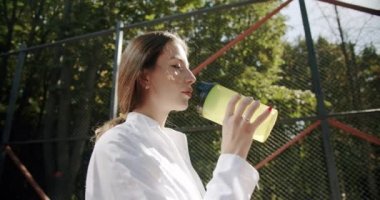 Genç ve güzel kız egzersizden sonra şişeden su içer.