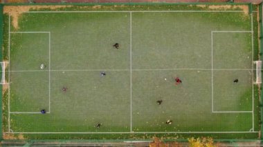 Yeşil futbol sahasında oynayan genç futbolcuların hava görüntüsü.