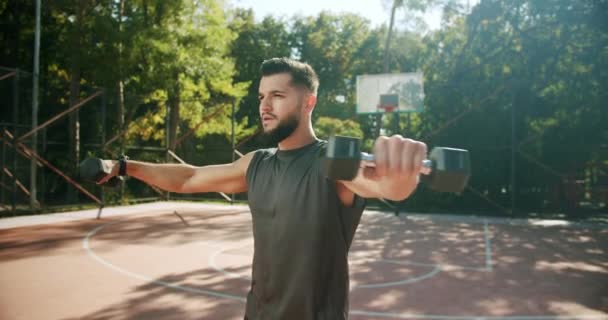 Мужчина поднимает тяжести обеими руками в общественном парке, тренируется по бицепсу — стоковое видео