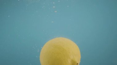 Sarı limonlar şeffaf suya dökülüyor mavi arka plan taze meyve turuncuları