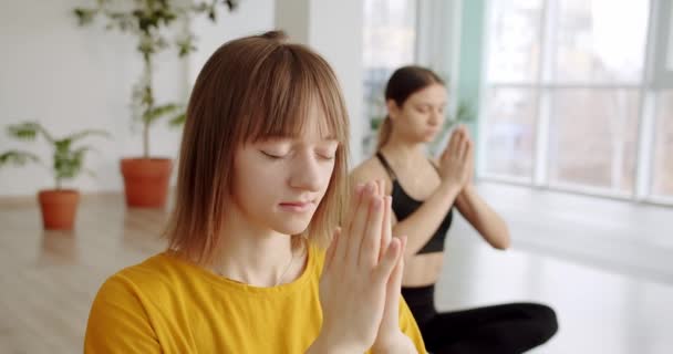 Mujeres jóvenes relajadas en ropa deportiva está meditando en posición de loto, clase de yoga — Vídeos de Stock