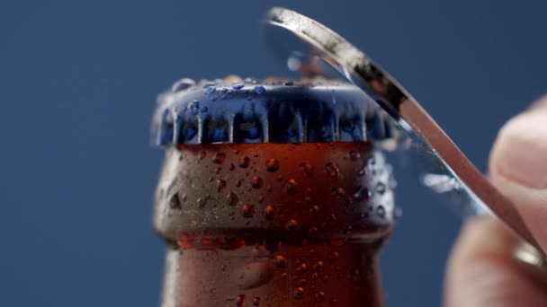 One hand opens the beer bottle on blue background. Close up, bottle opener — Stockvideo