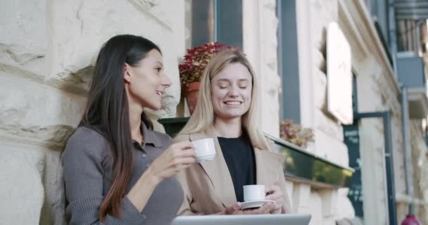 Twee meisjes rusten uit, serveren koffie en thee, praten en lachen buiten bij een terras — Stockvideo