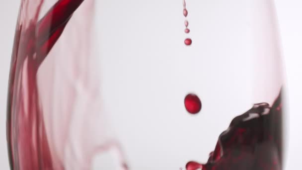 Sluiten Giet rode wijn in een glas op een witte achtergrond, in slow motion — Stockvideo