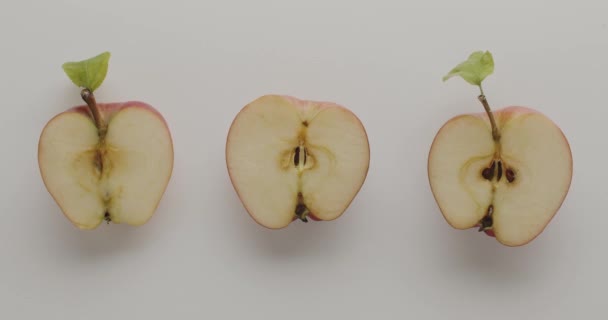 Group of three apples cut in half with leaves, on a white background with lights — Vídeo de stock