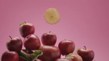 Birçok kırmızı elma ve bir dilim yavaşça elmaların üzerine iner, kırmızı-pembe arkaplan