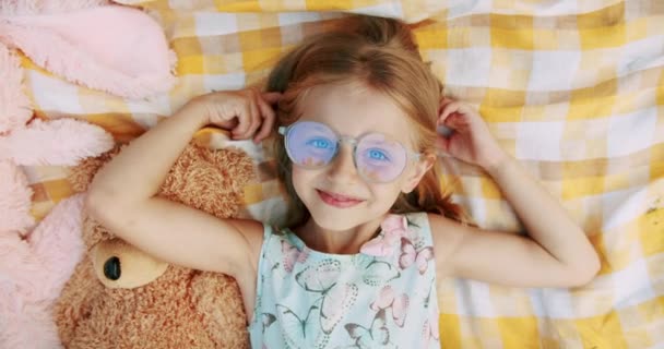 A little girl of 6-7 years with glasses, rests and sends greetings with her hand — Stockvideo