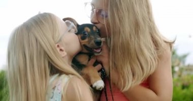 İki kız küçük bir köpeğe sarılıp öpüyor, dışarıda köpek yavrusuyla oynuyorlar.