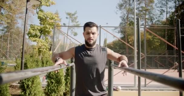 Homem muscular fazendo exercícios push-ups em barras paralelas, ABS, treino ao ar livre — Vídeo de Stock