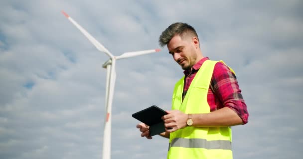 Inżynier pracuje obok turbin wiatrowych z tabliczką w ręku. — Wideo stockowe