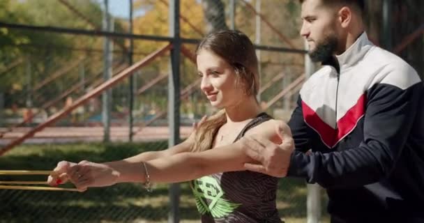 Sportieve vrouw met personal trainer doet oefeningen met weerstandsband buiten — Stockvideo