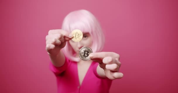 Die schöne Frau hält einen Bitcoin in der Hand, sie zeigt ihn aus nächster Nähe. Rosa Farbe — Stockvideo
