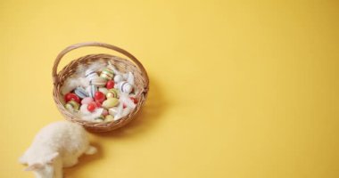 Sarı izole edilmiş arka planda beyaz tavşan bir sepet ve yumurtalarla oynuyor.