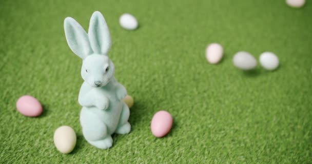 Juguete de conejo sobre un fondo de hierba verde con muchos huevos de colores, mensajes de texto — Vídeo de stock