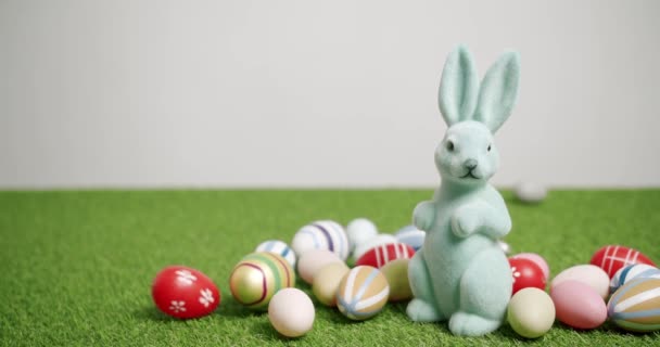 Juguete de conejo sobre un fondo blanco de hierba verde con muchos huevos de colores, Texto. — Vídeos de Stock