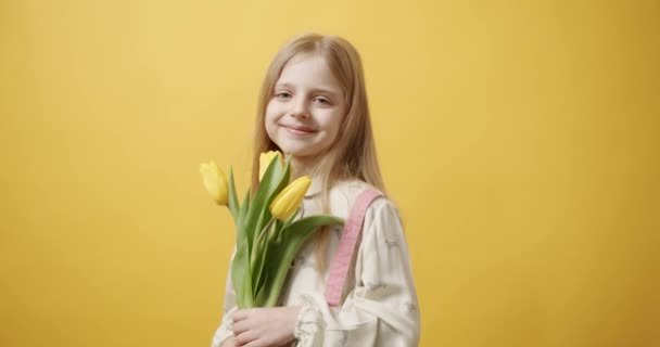 Hermosa chica sostiene flores de tulipán en su mano, sonríe sobre fondo amarillo — Vídeo de stock