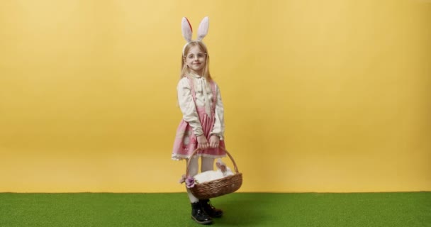 Mała dziewczynka w różowej sukience trzyma koszyk z królikiem w dłoni, pozowanie, uśmiech — Wideo stockowe