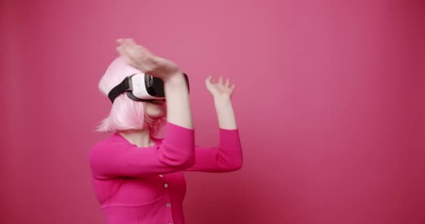 Kvinna använder en virtuell verklighet glasögon på isolerad rosa bakgrund — Stockvideo