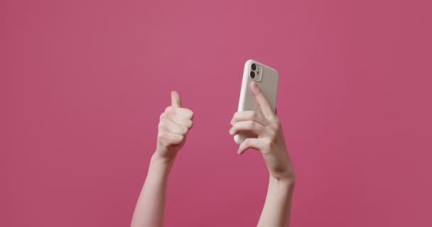 De jonge vrouw maakt gebruik van een SmartPhone en toont de Like symbool op roze achtergrond — Stockvideo