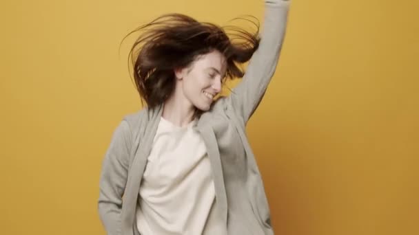 Mujer sonriendo bailando con música rítmicamente para vencer moviéndose sobre fondo amarillo — Vídeos de Stock