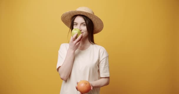 Den vackra damen luktar ett äpple och en apelsin, kramar dem på gul bakgrund — Stockvideo