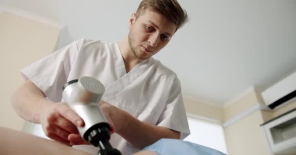 Médico que trata los músculos de la espalda de los pacientes con dispositivo de percusión de masaje — Vídeo de stock