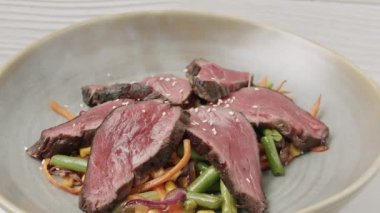 Izgara sebze salatasını beyaz tabakta az pişmiş biftekle kapat.. 