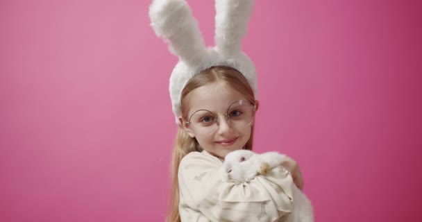 Dziewczynka z króliczymi uszami, królik w ręku, pozująca i uśmiechnięta. Tekst sztandaru — Wideo stockowe