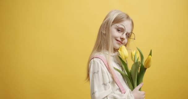 Menina bonita segura flores de tulipa em sua mão, ela sorri no fundo amarelo — Vídeo de Stock