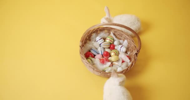 Two White rabbits on a yellow isolated background plays with a basket and eggs — Stock Video