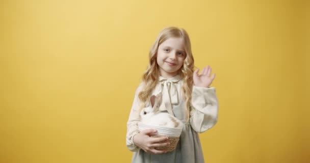 Το κοριτσάκι χαμογελάει με ένα λευκό φόρεμα κρατά ένα καλάθι με ένα κουνέλι στα χέρια της — Αρχείο Βίντεο