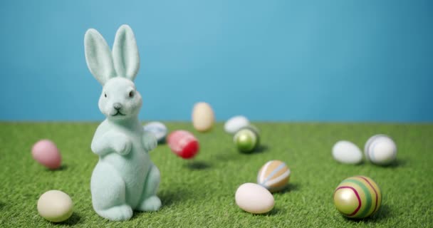 Rabbit Toy on a Blue Background of Green Grass with many colored eggs, Text. — Stock Video