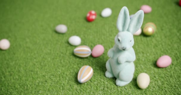 Кроличья игрушка на фоне зеленой травы с множеством цветных яиц, текстовые сообщения — стоковое видео