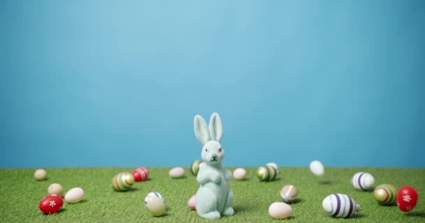Kanin leksak på en blå bakgrund av grönt gräs med många färgade ägg, Text. — Stockvideo