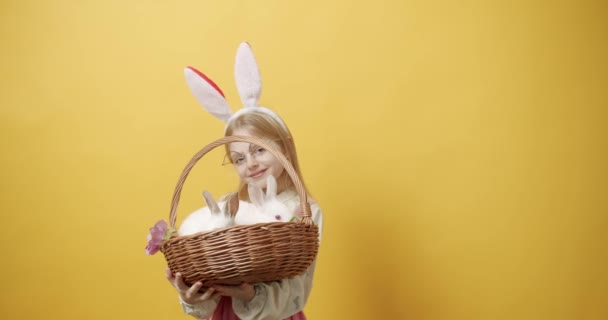 Dziewczynka uśmiecha się z króliczymi uszami, trzyma kosz z królikiem w rękach — Wideo stockowe