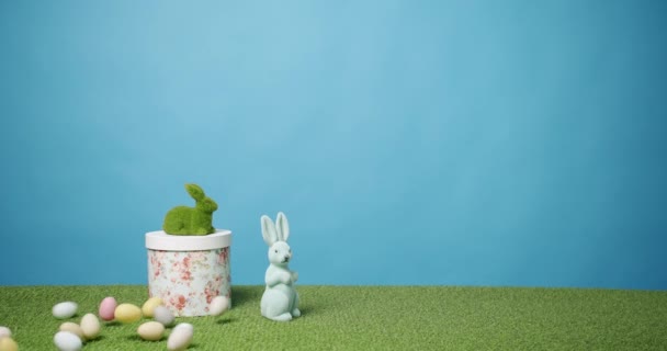 Kanin leksak på en blå bakgrund av grönt gräs med många färgade ägg, Text. — Stockvideo