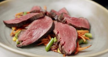 Izgara sebze salatasını beyaz tabakta az pişmiş biftekle kapat.. 