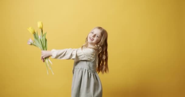 Menina bonita segura flores de tulipa em sua mão, ela sorri no fundo amarelo — Vídeo de Stock