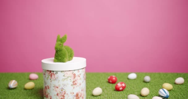 Rabbit Toy egy rózsaszín háttér zöld fű sok színes tojás, Szöveg. — Stock videók