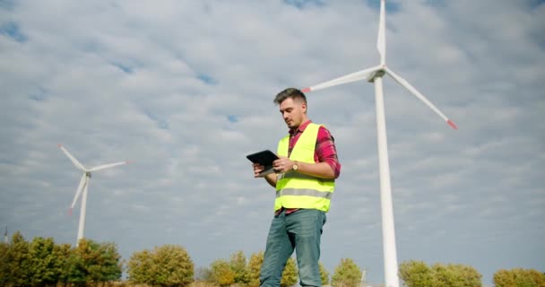 De ingenieur werkt naast de windmolens met de tablet in zijn hand — Stockvideo