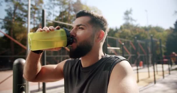 Atleta relaxante e bebe água da garrafa após um treino intenso. — Vídeo de Stock