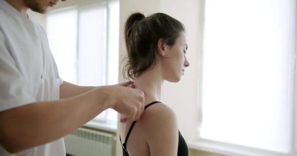 Az orvos egy nőt kezel cumisüveggel a hátán egy klinikán.. — Stock videók