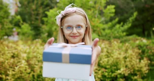 Krásná sedmiletá dívka s brýlemi, dát dárek v modré krabici s lukem. — Stock video