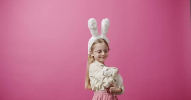 Tavşan kulaklı küçük bir kız, elinde bir tavşan, poz veriyor ve gülümsüyor. Sancak Metni — Stok video