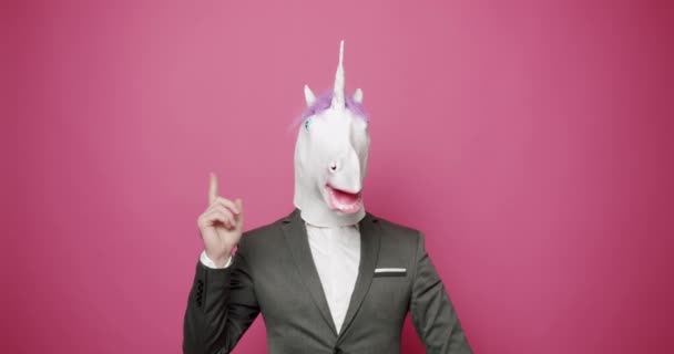 Il tizio in giacca e cravatta grigia con maschera unicorno ha una buona idea. dimostra e guarda — Video Stock