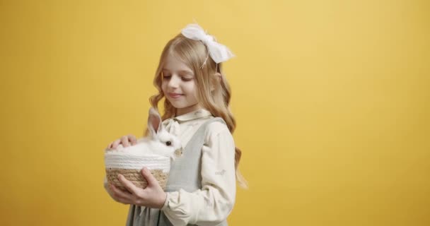 Liten flicka ler i en vit klänning håller en korg med en kanin i händerna — Stockvideo