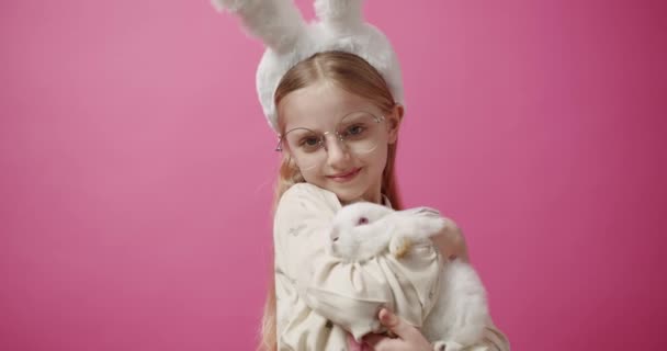 Tavşan kulaklı küçük bir kız, elinde bir tavşan, poz veriyor ve gülümsüyor. Sancak Metni — Stok video